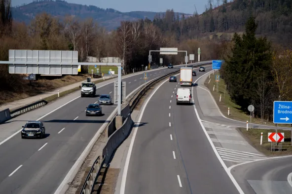 Slovakia D3 motorway near Žilina-Brodno with mixed traffic including trucks and cars, blue directional sign for Katowice, Ostrava and Kysucké Nové Mesto visible, enforcement gantry overhead and forested mountains in background, February 2026
